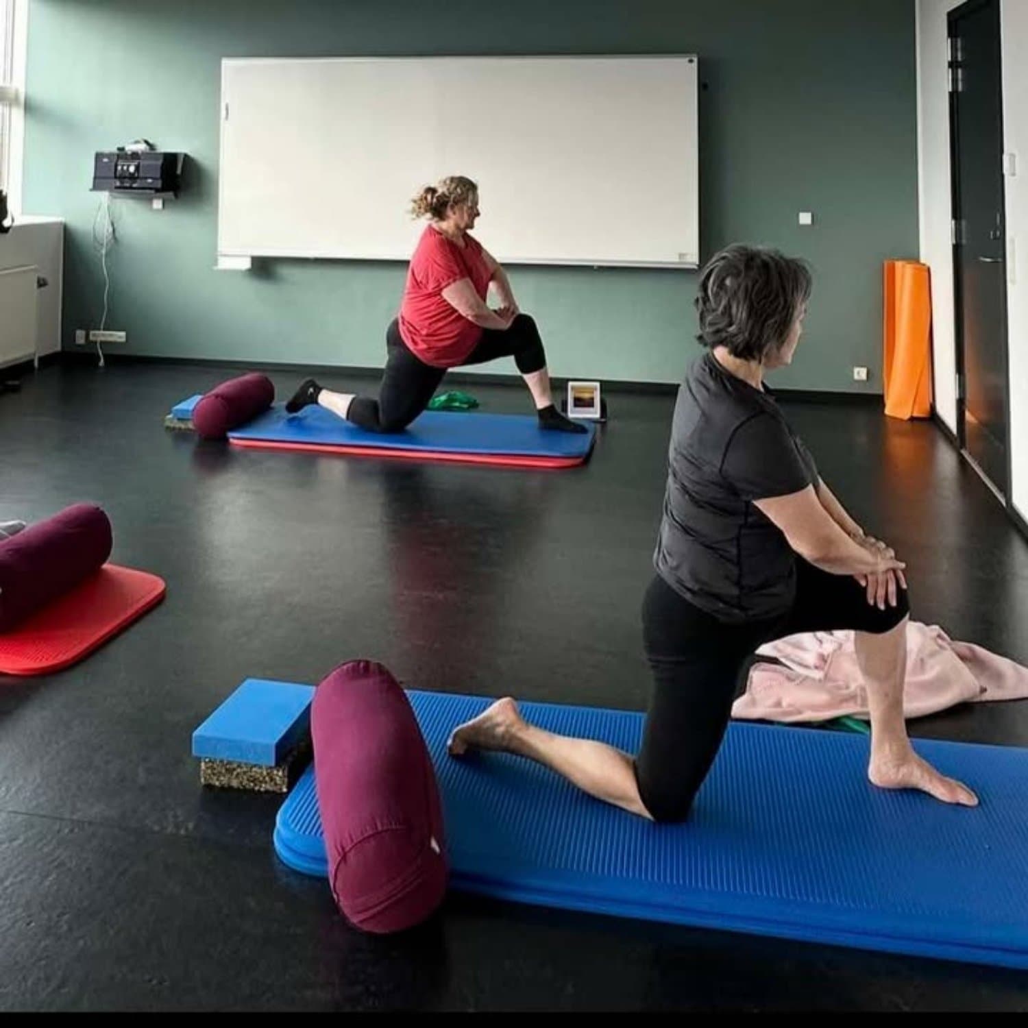 Tina Knudsen der underviser kursister i pilates på yogamåtter iført afslappet træningstøj i FOF's lokaler på KUC i Kolding