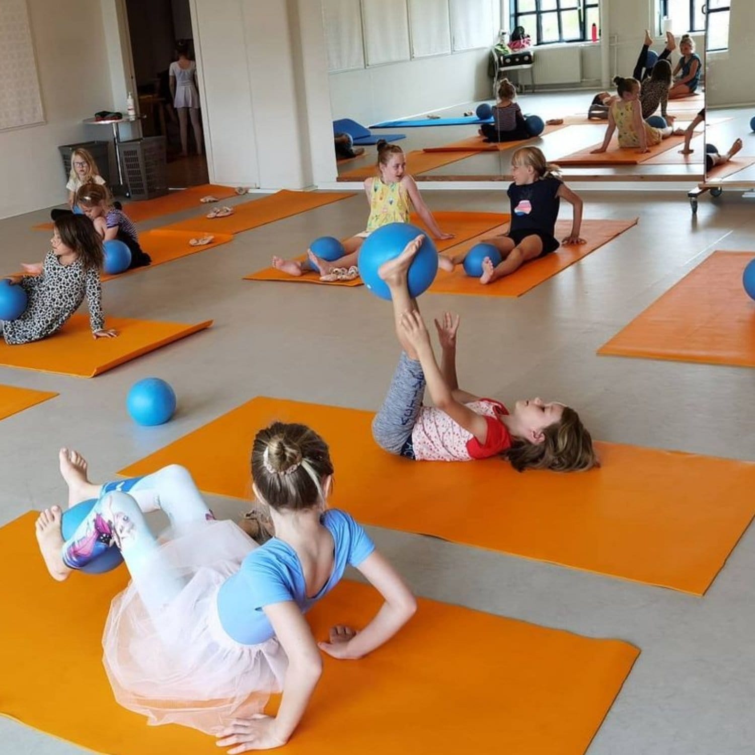 Balletbørn der laver øvelser med bolde på måtter