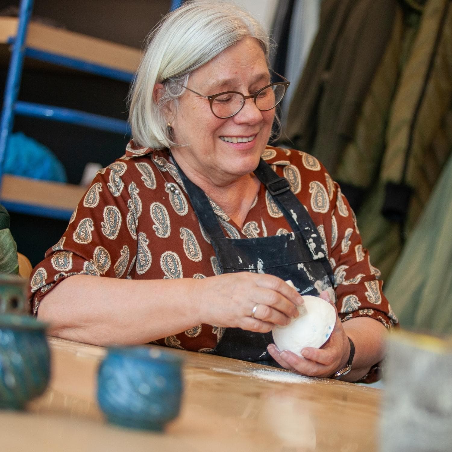 Kursist med forklæde på der behandler et keramikværk i keramikværkstedet på KUC i Kolding