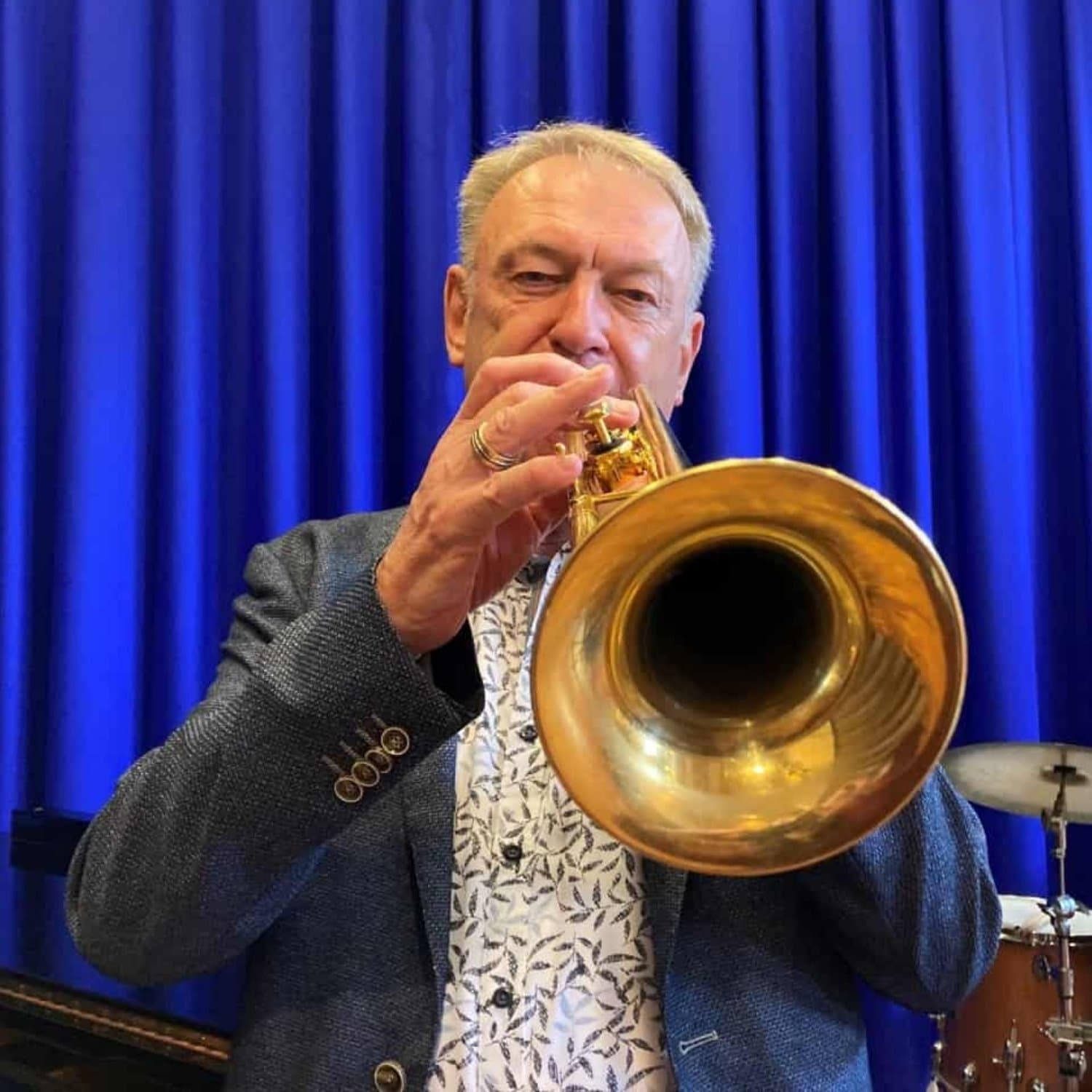 Kurt Holm der spiller på trompet i jakkesæt med blåt forhæng i baggrunden